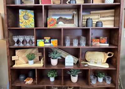 bookcase filled with cutting boards, glasses, and fake plants image